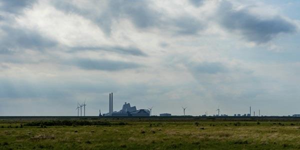 Green grass field under white clouds at day time. Windmills and industrial building in background.