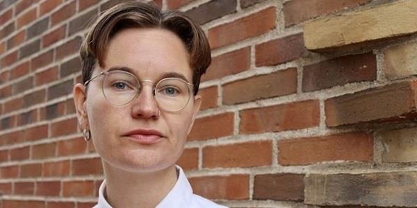 Person with glasses in a white shirt in front of a brick wall