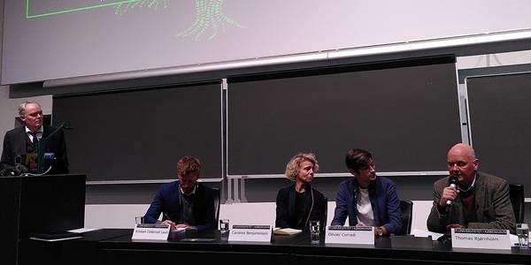 Five people in an auditorium engaged in debate