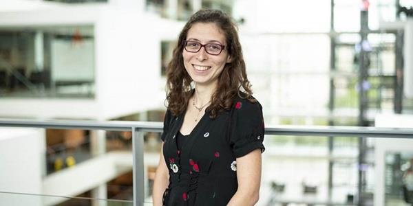 Woman in black t-shirt with long hair and glasses standing inside indoor atrium