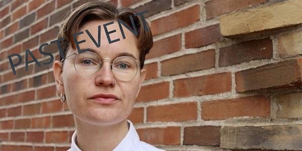 Person in white shirt and glasses with short hair in front of brick wall