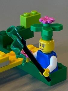 Lego figure with a pink flower on its head, holding a green flag