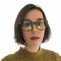 Headshort of white woman with short brown hair, a kaki jumper, big glasses and red lipstick, against a white background.