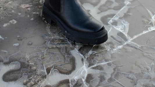 picture of black boot breaking the ice covering a shallow puddle