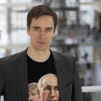 Leon has short dark hair, a black blazer and a t shirt with print